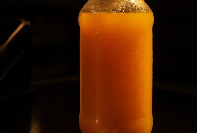 A clear bottle of orange juice beside dollar bills on a dark grocery checkout counter