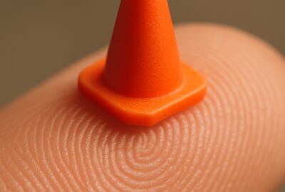 Tiny orange Playmobil traffic cone balanced on a human fingertip showing miniature scale