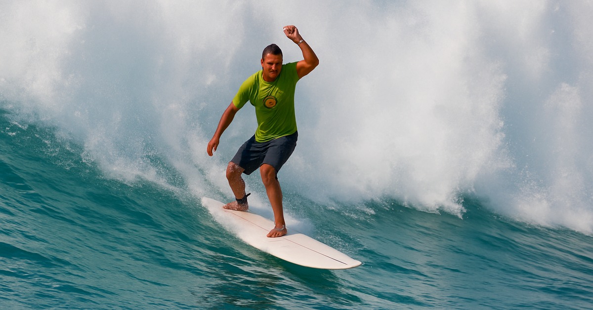 Low waterline angle of surfer on white longboard with towering whitewater wall behind