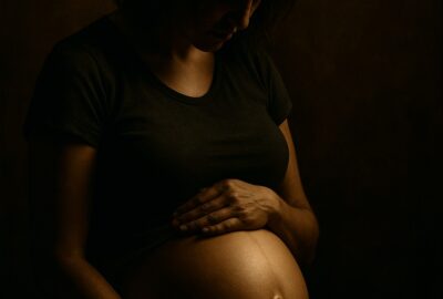Pregnant woman in dark studio light cradling her bare belly with both hands tenderly