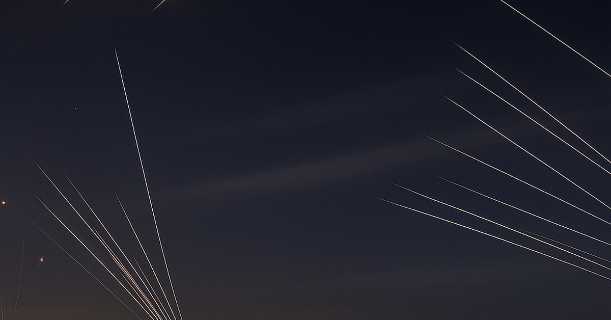 Multiple missile intercept light trails fan outward over an amber-lit urban horizon at night