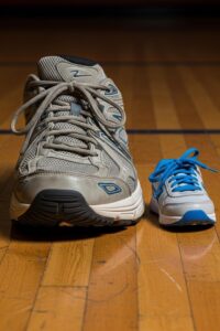 A towering basketball player's sneaker beside a small child's shoe on a wooden floor
