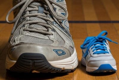 A towering basketball player's sneaker beside a small child's shoe on a wooden floor