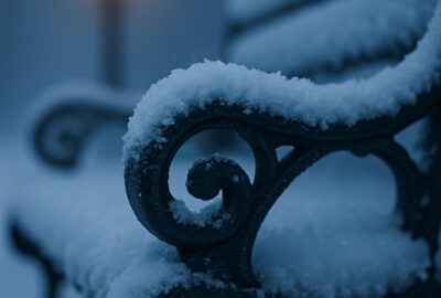 Snow-laden cast-iron park bench beside glowing Victorian lamp post on foggy winter path