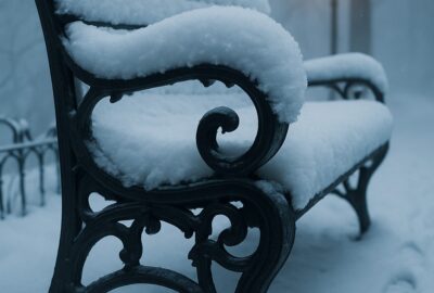Snow-covered Victorian park bench and glowing lamp post in silent winter storm