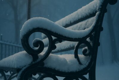 Snow-covered Victorian park bench and glowing amber street lamp in winter fog