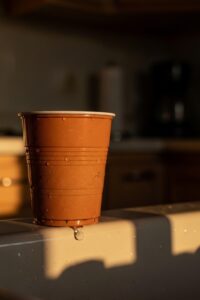 A small orange plastic cup sitting alone on a kitchen sink at dusk, bathed in soft golden light