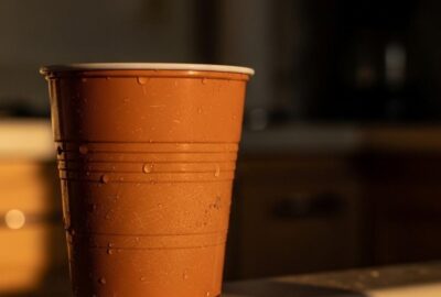 A small orange plastic cup sitting alone on a kitchen sink at dusk, bathed in soft golden light