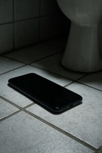 Close-up of a smartphone resting on a bathroom floor beside a toilet base