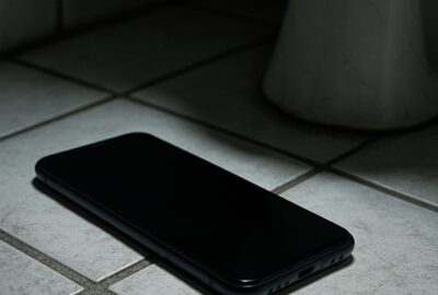 Close-up of a smartphone resting on a bathroom floor beside a toilet base