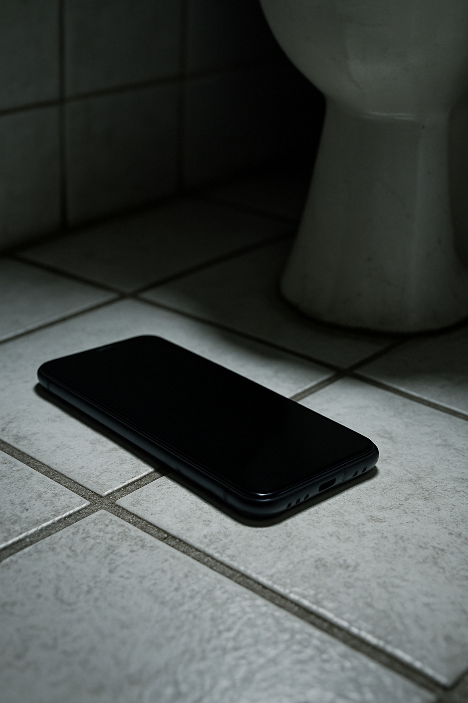 Close-up of a smartphone resting on a bathroom floor beside a toilet base