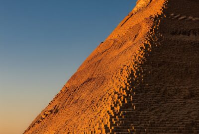 The Great Pyramid of Khufu rising against a deep blue Egyptian sky at golden hour, weathered limestone glowing warm amber