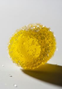 A single vivid yellow sour hard candy coated in sparkling sugar crystals, extreme close-up on a clean neutral surface, b