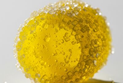 A single vivid yellow sour hard candy coated in sparkling sugar crystals, extreme close-up on a clean neutral surface, b