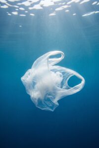 A translucent plastic bag drifting in blue open ocean water resembling a floating jellyfish
