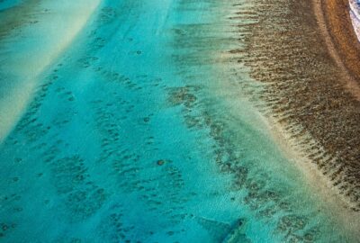 Shallow turquoise lagoon of a remote coral atoll with a faint elongated metallic shape beneath the clear water near the reef edge