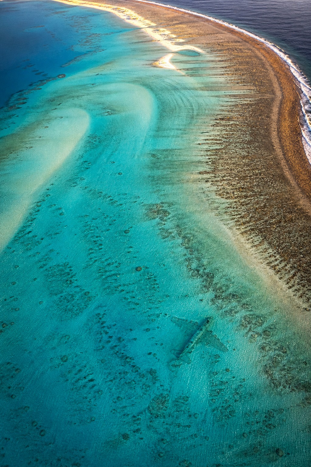 Ondiepe turquoise lagune van een afgelegen koraalatol met een vage langwerpige metaalachtige vorm onder het heldere water nabij de riffrand