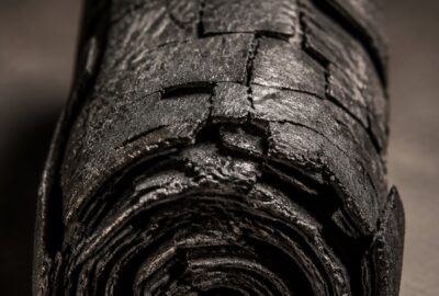 A blackened, carbonised Herculaneum papyrus scroll fused solid, lit dramatically against a dark background