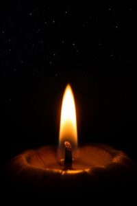 A single lit candle flame glowing against deep darkness, surrounded by faint stars on a moonless night