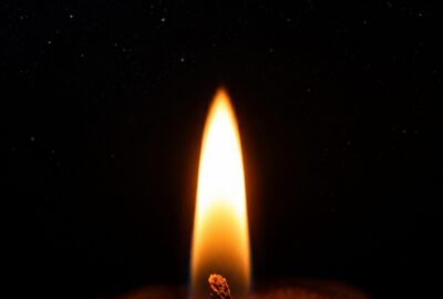 A single lit candle flame glowing against deep darkness, surrounded by faint stars on a moonless night