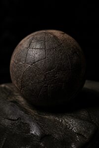 Ancient dark rubber ball from the Olmec site of El Manatí, its cracked surface lit dramatically against a black background