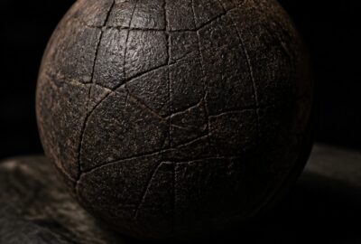 Ancient dark rubber ball from the Olmec site of El Manatí, its cracked surface lit dramatically against a black background