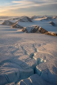Vast blue Antarctic ice sheet meeting dark rock under low golden polar light, symbolising the continent's protected, mineral-rich interior