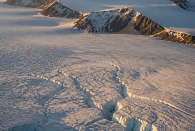Vast blue Antarctic ice sheet meeting dark rock under low golden polar light, symbolising the continent's protected, mineral-rich interior