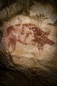 The world's oldest story cave painting: a faded red-ochre scene of a Sulawesi warty pig and human-like figures on a limestone cave ceiling at Leang Karampuang